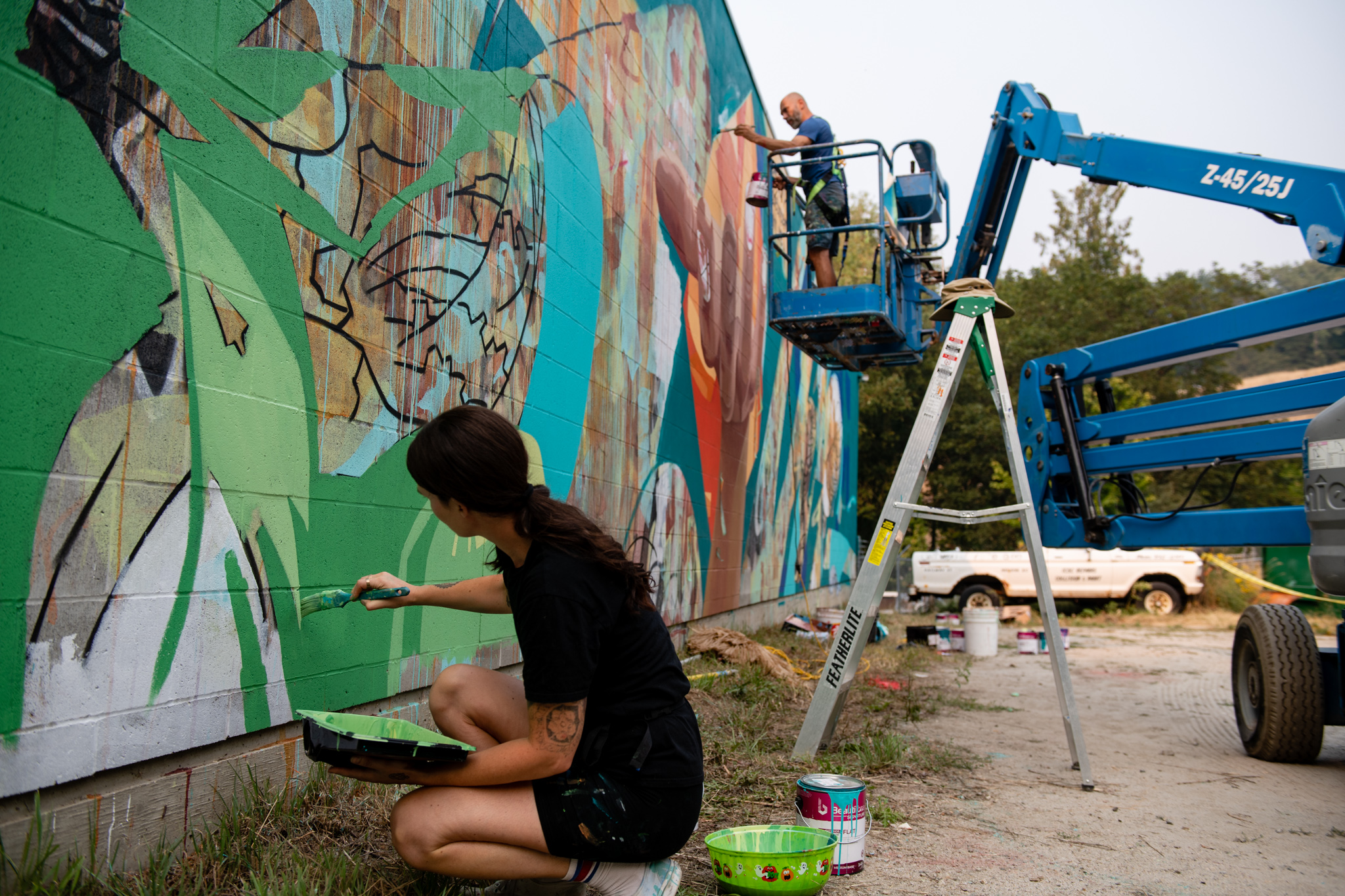 Two muralists painting green lines